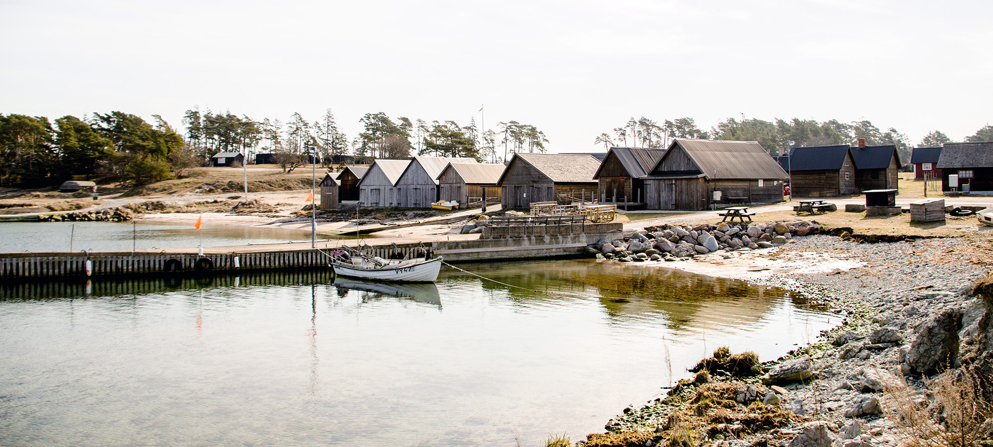 Stugor, strand och båt liggandes i vackra Djupviks Hamn på Gotland